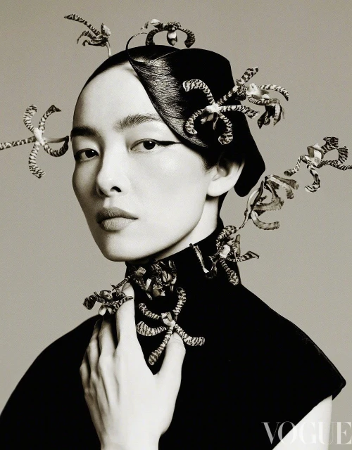Headshot of an Asian woman wearing a black turtleneck and decorative head and neck piece posing in a photo studio against a grey backdrop.
