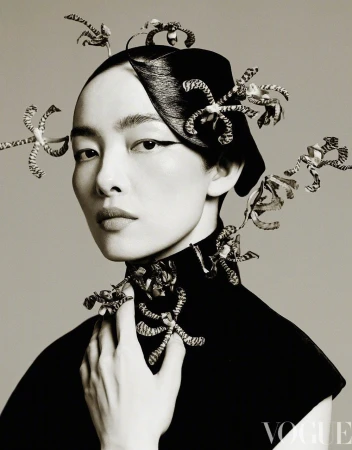 Headshot of an Asian woman wearing a black turtleneck and decorative head and neck piece posing in a photo studio against a grey backdrop.