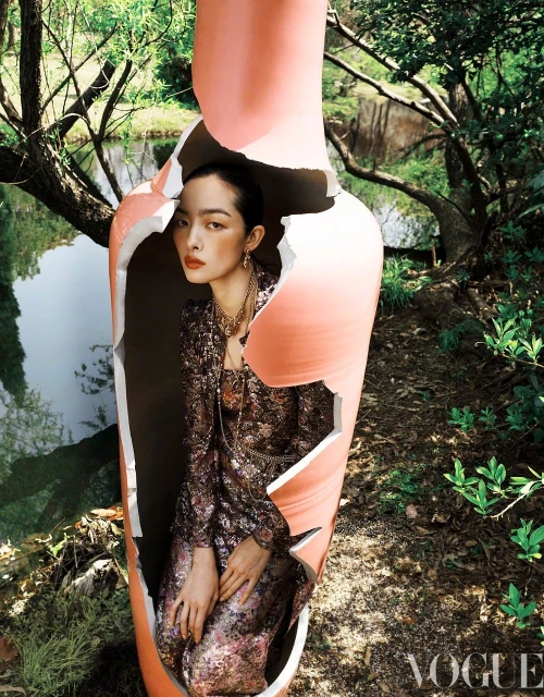 Artistic fashion portrait of an Asian woman inside a cracked peach vase, against a backdrop of trees and a body of water.