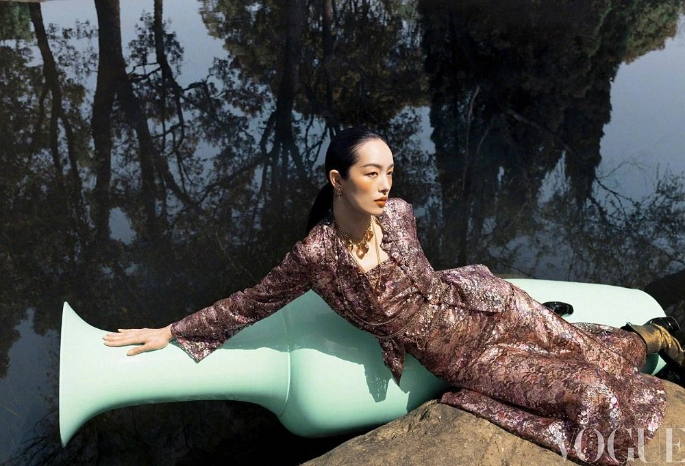 Model FeiFei Sun lounging on a large mint green ceramic vessel next to water for Vogue China