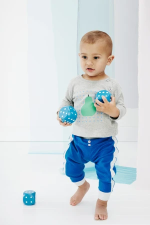 A toddler wearing blue pants and a grey shirt holds blue polka-dotted dice in a white photo studio with translucent blue panels.