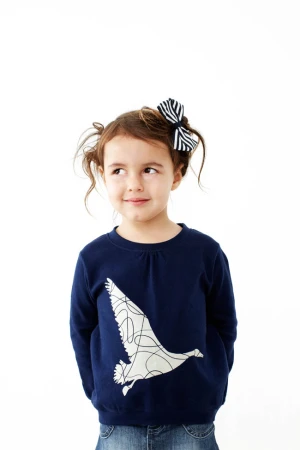 Adorable young girl with pigtails wearing a navy sweatshirt with bird design and jeans against a white background in a studio shot.