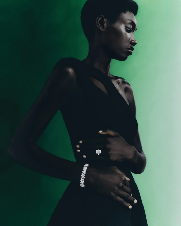 Black woman wearing a dark dress, diamond bracelet, and ring against a gradient green background for Harrods.