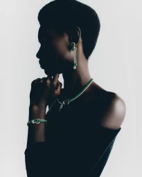 Profile portrait of a Black model wearing emerald jewellery and a necklace against a seamless white background.