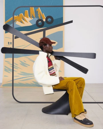 Model seated on a black chair carrying black skis with an illustrated mountain backdrop for Marni Magic Mountain
