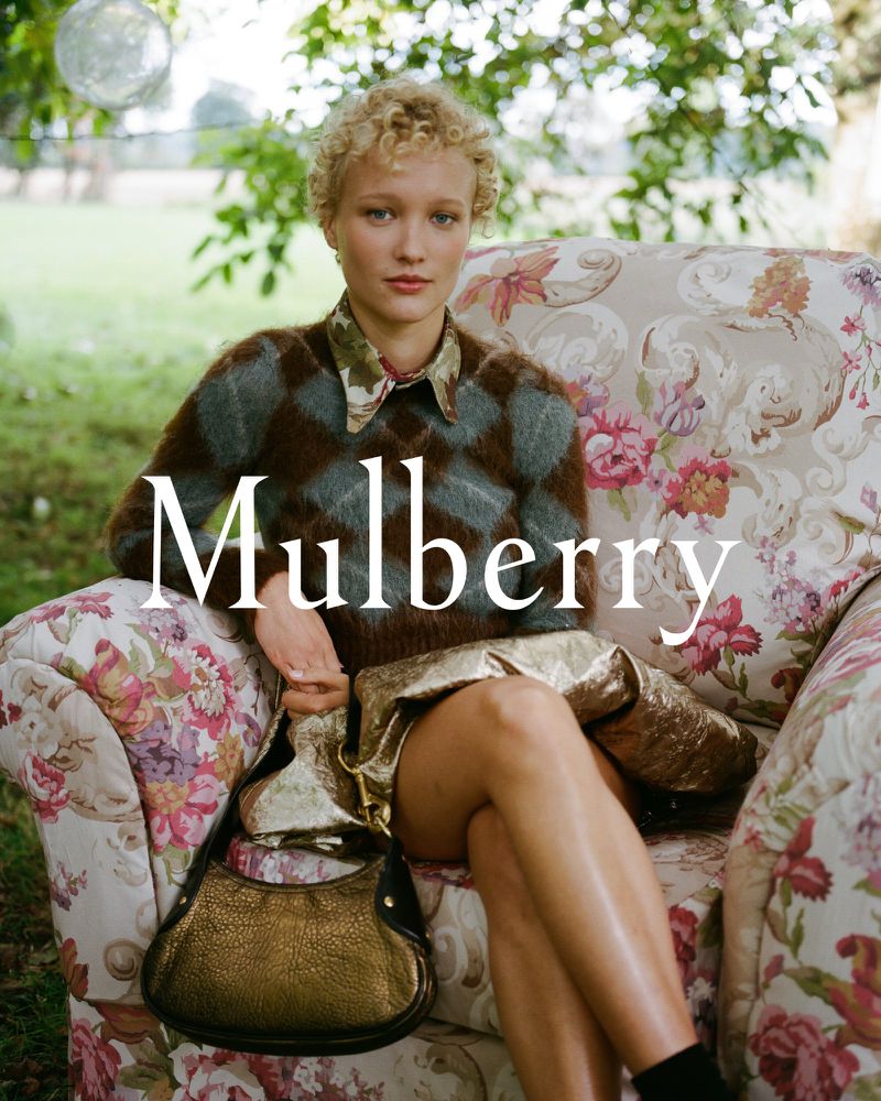 Fashion editorial shot of a blond woman posing with a metallic purse in an outdoor setting, floral chair, and a 'Mulberry' logo overlay.