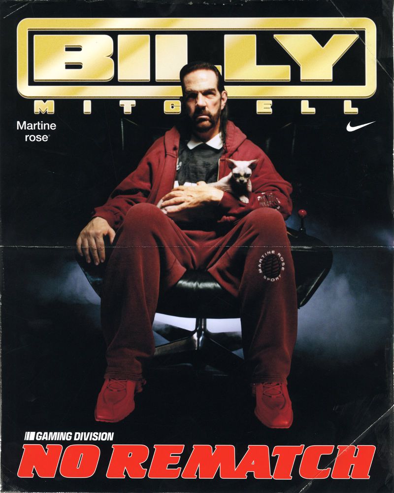 Billy Mitchell sits in a black leather chair, cradling a small dog, wearing a red sweatsuit and matching sneakers on a magazine cover.