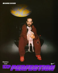 Man seated in a black chair holding a hairless cat, wearing a burgundy fleece tracksuit and red sneakers for Nike x Martine Rose.