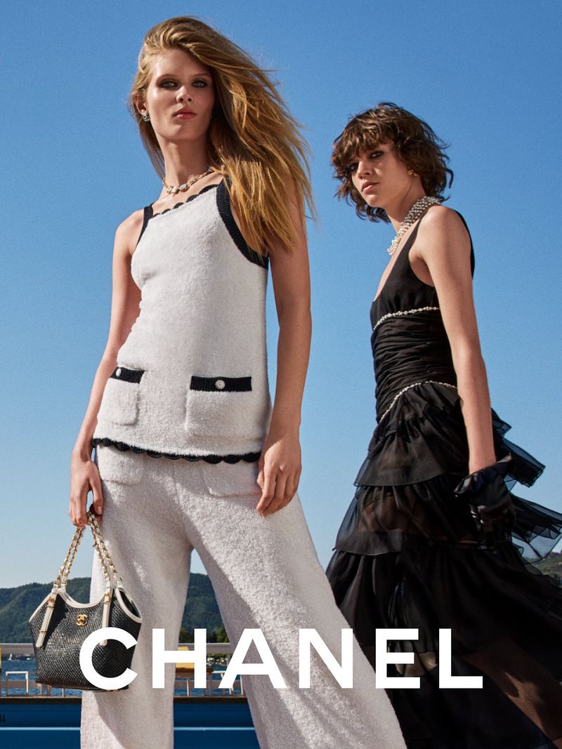 Two fashion models in Chanel clothing pose outdoors against a blue sky, featuring a handbag, jewelry, and a modern, elegant aesthetic.