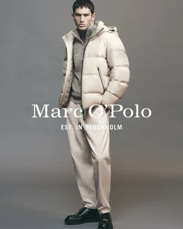 Model Luka Tesic wearing a cream hooded puffer jacket and beige trousers against a neutral grey studio backdrop.