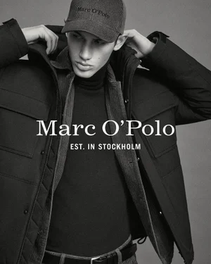 Model Luka Tesic wearing a black hooded winter jacket, layered knitwear, and a branded baseball cap in a black and white portrait.