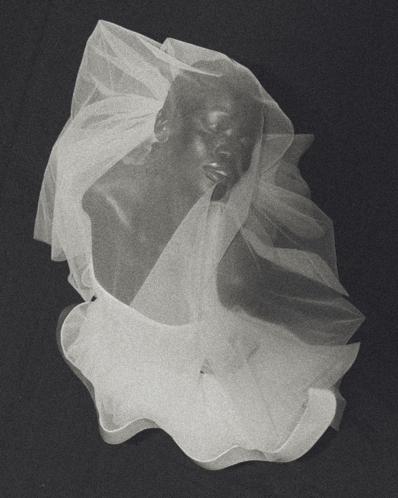 Artistic portrait of an African American adult woman wearing a white veil against a dark background in a studio setting.