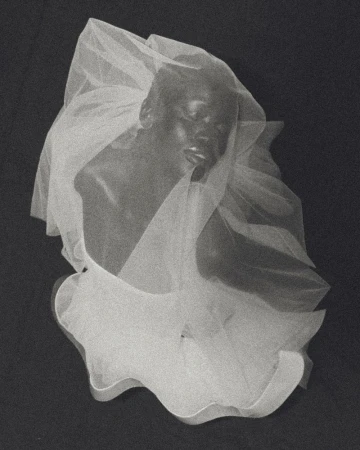 Artistic portrait of an African American adult woman wearing a white veil against a dark background in a studio setting.