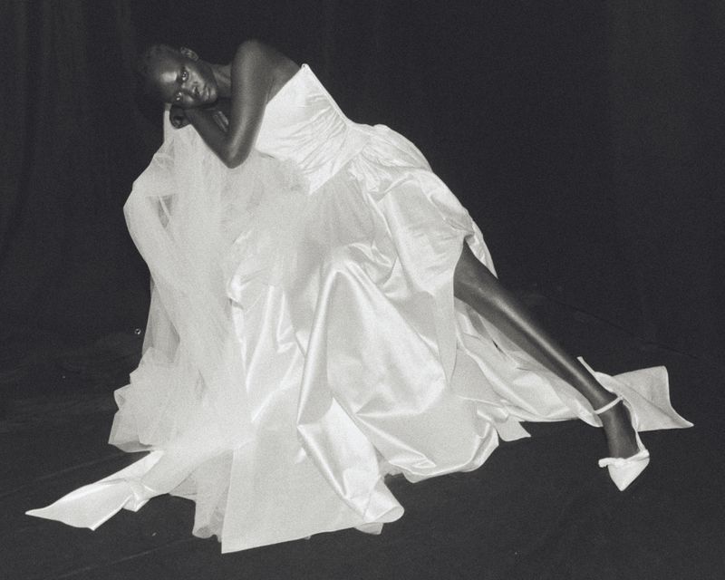 Model reclining in a voluminous strapless white satin bridal gown against a black studio backdrop for Wed Studio.