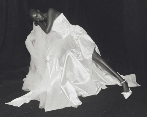 Model reclining in a voluminous strapless white satin bridal gown against a black studio backdrop for Wed Studio.