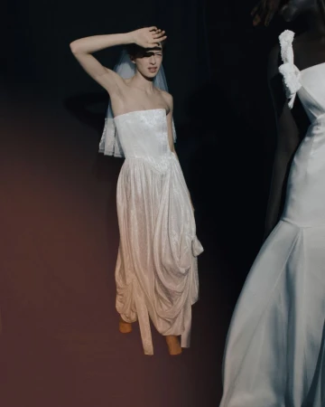 Two women pose wearing wedding dresses against a dark backdrop in a studio setting, illuminated by focused lighting to highlight their attire.