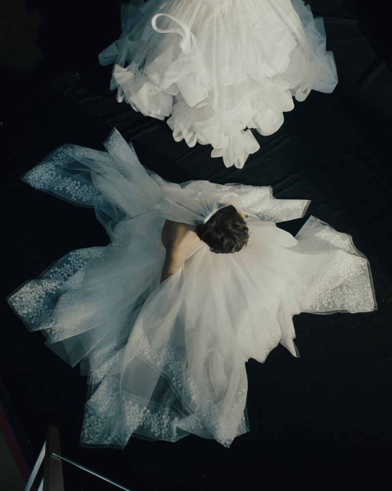 Overhead shot of a person in a white dress with a voluminous skirt, under another similar dress, against a dark background.