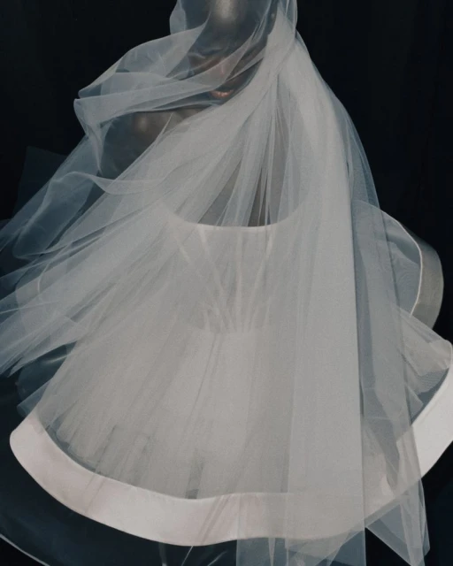 Close-up shot of a mannequin draped in a flowing white tulle veil, with a black backdrop creating a dramatic studio effect.