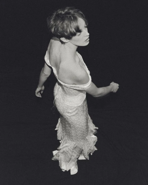 Monochrome portrait of a slender woman with short hair wearing an open-back dress, with a black backdrop in a studio setting.