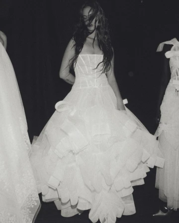 Monochrome image of a woman in a white strapless gown with a ruffled skirt, posing between two other similarly-dressed women in gowns.