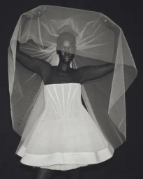 Black model wearing a strapless white corset mini dress and holding an expansive sheer bridal veil against a black background.