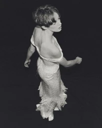 High-angle view of a woman in a textured white off-the-shoulder bridal gown with a ruffled hem against a black studio background.