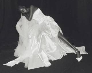 Model reclining in a voluminous strapless white satin bridal gown against a black studio backdrop for Wed Studio.