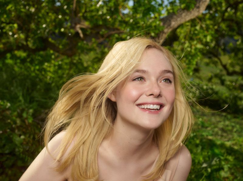 Blonde woman smiling outdoors against green leafy trees. Portrait of a fair-skinned woman with long blonde hair in a natural setting.