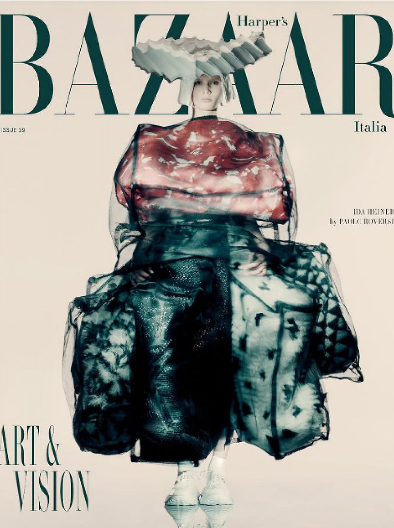 Fashion editorial featuring a model in a translucent dress and avant-garde headpiece, styled for Harper's Bazaar Italia, studio shot.