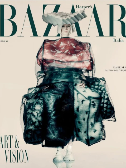 Fashion editorial featuring a model in a translucent dress and avant-garde headpiece, styled for Harper's Bazaar Italia, studio shot.