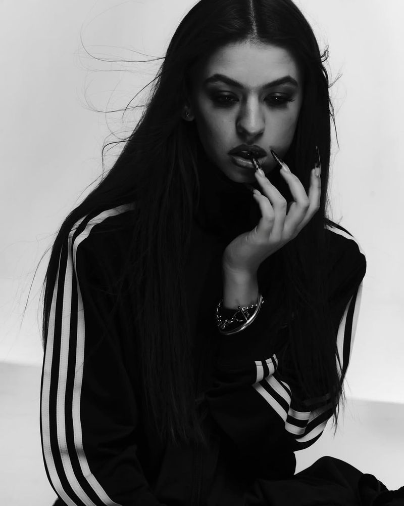 Dramatic black-and-white portrait of a woman with long dark hair and long nails, wearing a black turtleneck sweatshirt with white stripes.