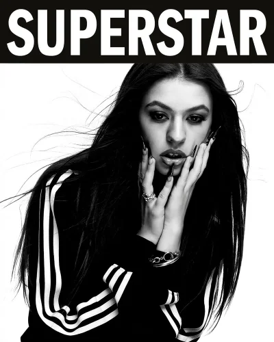 Monochrome portrait of a woman in an Adidas three-stripe track jacket posing with hands to face beneath Superstar text.