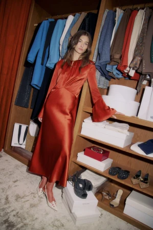 Fashion shoot of a woman in a copper dress in a closet, surrounded by clothes, shoes, and purses for a sophisticated aesthetic.
