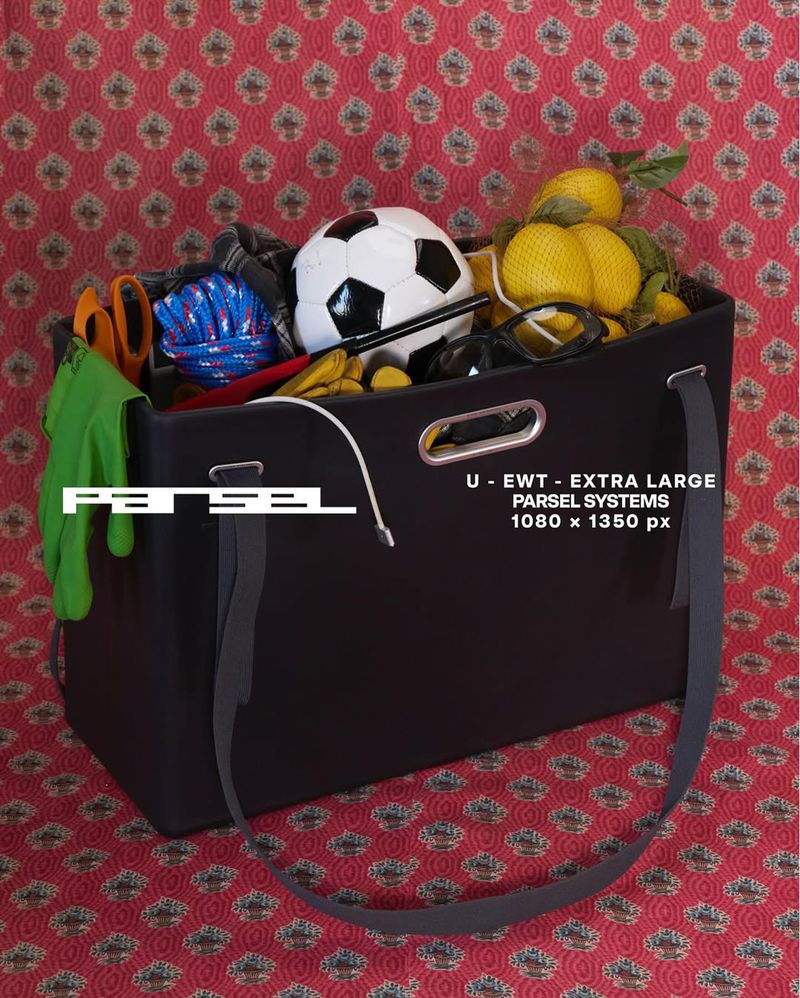 Black tote bag overflowing with sports equipment, garden gloves, and lemons on a red patterned background in a studio setting.