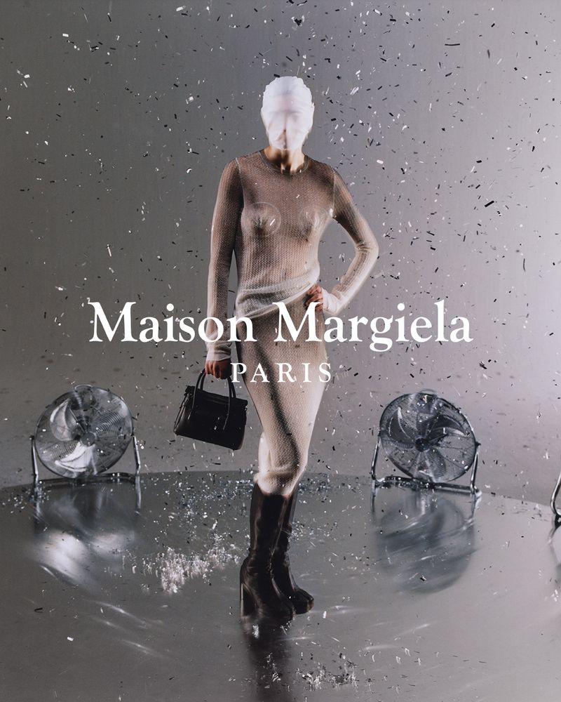 Fashion shot of a model in a shimmering dress and boots, holding a purse, with fans and confetti against a silver backdrop.