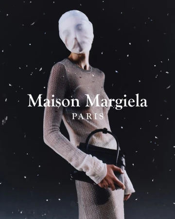 Fashion shot of a woman wearing a translucent, full-length dress and a head covering, holding a black purse against a dark background.