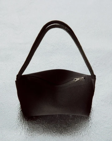 Studio shot of a simple, black fabric handbag with black straps, featuring a zippered pocket, set against a shiny, silver background.