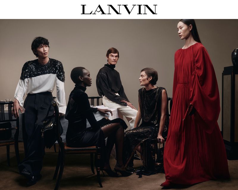 Fashion editorial featuring five diverse models in black, white, and red designer outfits in a minimalist studio setting with soft lighting.