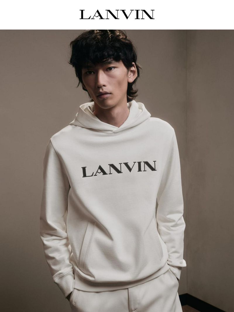 An adult male model poses indoors wearing an off-white hooded sweatshirt with 'LANVIN' printed on the front and matching pants.