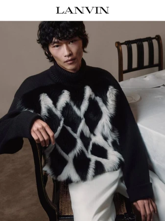 Model Bai wearing a black Lanvin turtleneck sweater with a textured diamond pattern seated beside a dining table.