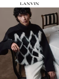 Model Bai wearing a black Lanvin turtleneck sweater with a textured diamond pattern seated beside a dining table.