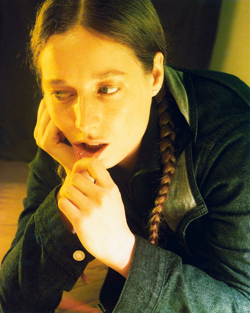 Portrait of a woman with a braid and denim jacket, illuminated with warm lighting, in an intimate, close-up studio setting.