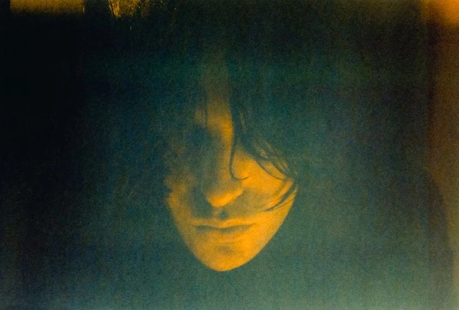 Close-up portrait of a woman with long dark hair, lit with a warm yellow glow, creating a dramatic and intimate atmosphere.