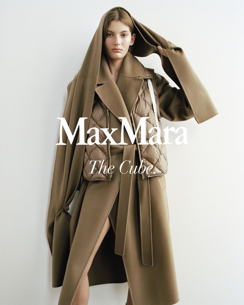 Model wearing a brown belted coat and quilted puffer vest with matching hood against a white wall