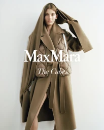 Model wearing a brown belted coat and quilted puffer vest with matching hood against a white wall