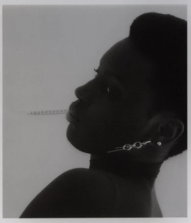Monochromatic studio shot of a black woman in profile with modern chain earrings and a measuring stick as a prop in her mouth.
