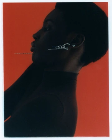 Profile portrait of a Black woman wearing silver earrings against a vibrant red background for Justine Clenquet Reedition