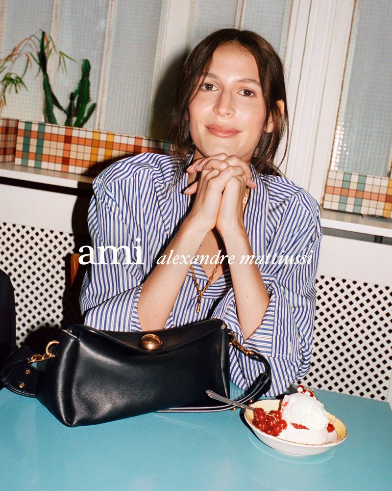 Portrait of a woman with a black purse on a table next to a dish of ice cream with red berries in an indoor setting.