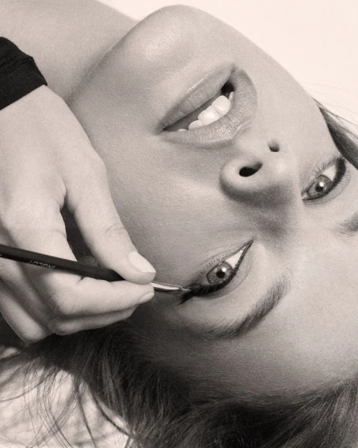 Close-up shot of a model getting her eyeliner applied by a makeup artist with a thin brush in a beauty studio, monochrome.