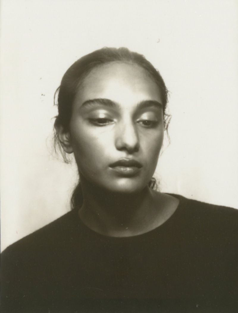 Portrait of a young adult woman in front of a plain white background, wearing a black top and hair pulled back in a simple style.